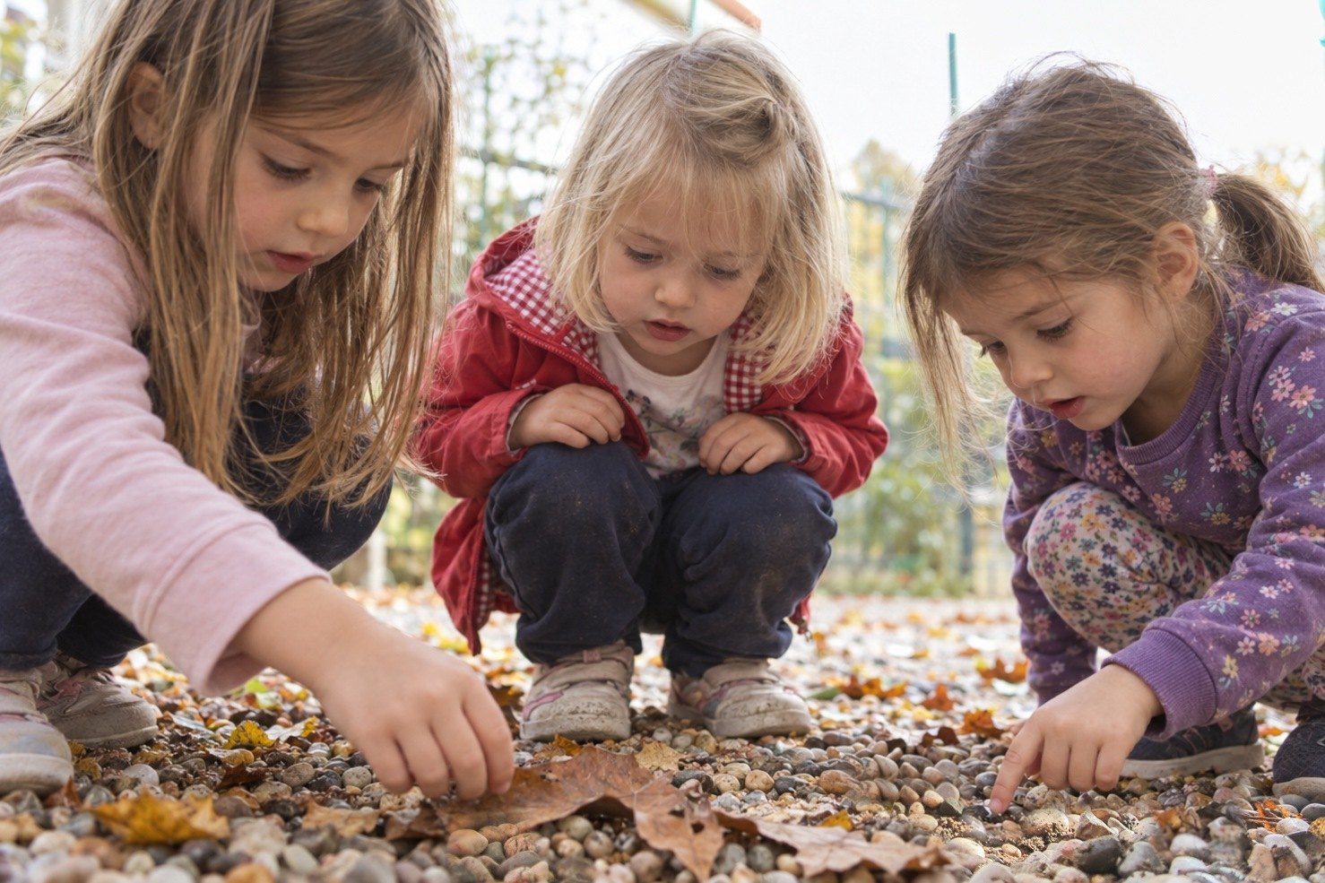 Bambine dell’infanzia accucciate in giardino che esplorano foglie e sassolini