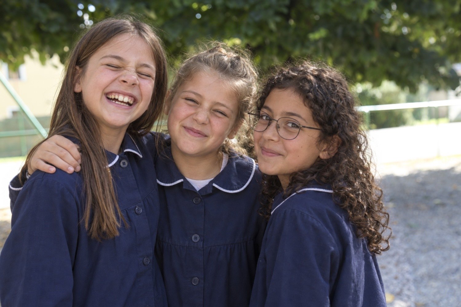 Tre amiche della primaria con il grembiule, abbracciate in cortile